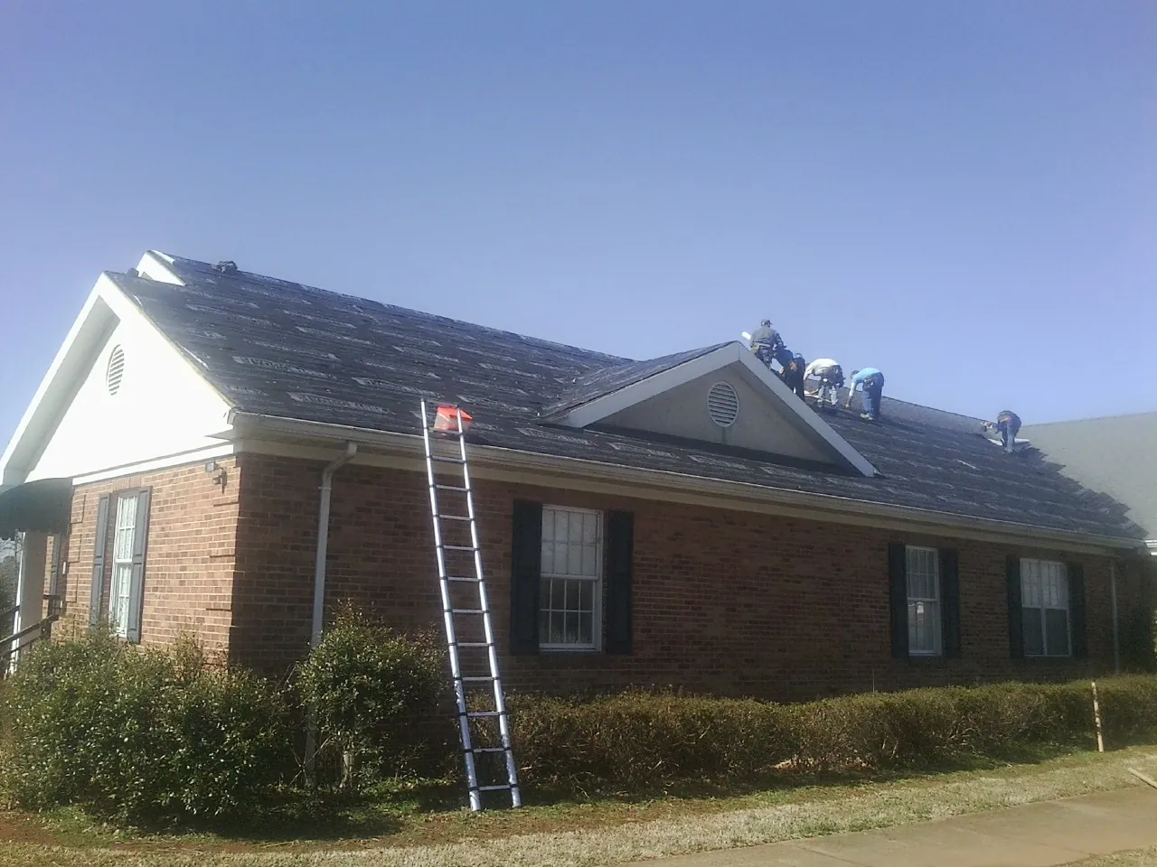 Crew tearing shingles off a brick ranch roof with a ladder set — Metal Roof Repair work by our crew in Smoketown