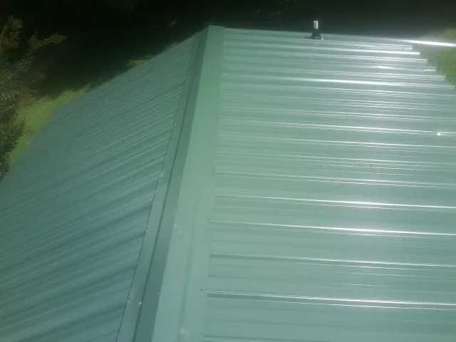 New green metal panels meeting at the ridge of a roof — Flat Roof Repair work by our crew in Smoketown