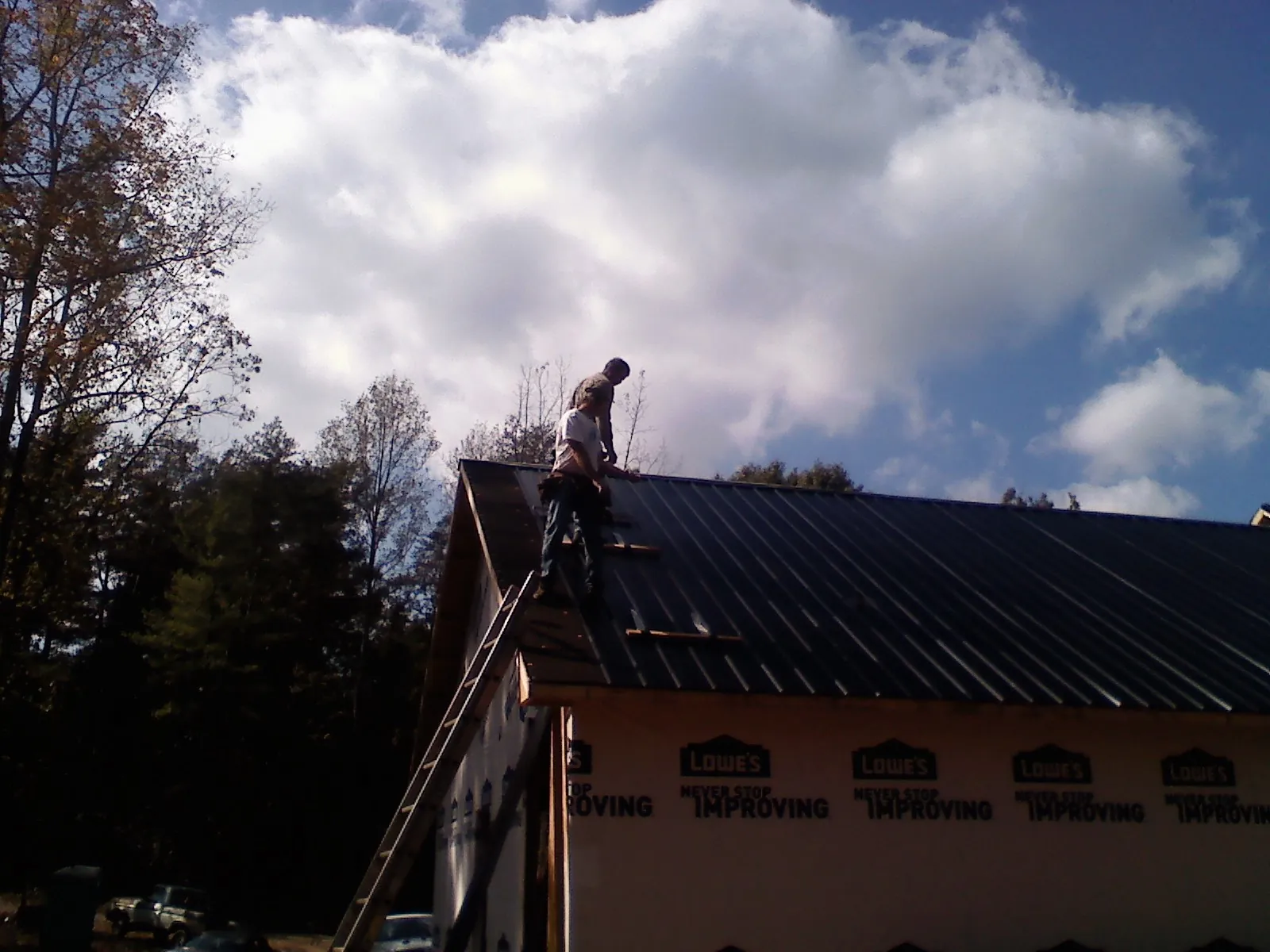 Roofer fastening dark metal panels high against a cloudy sky, from a Roof Inspection job in Smoketown