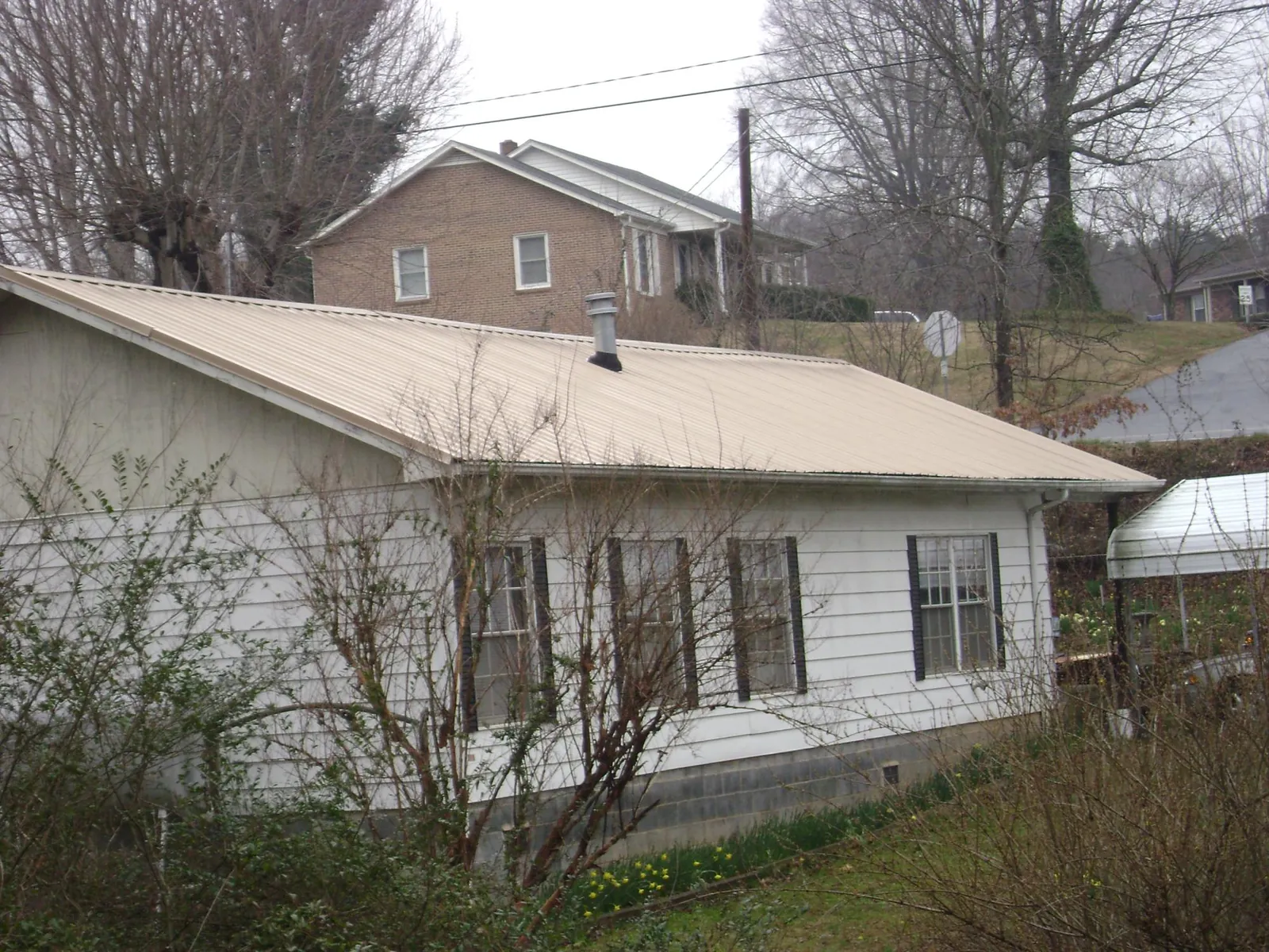 Tan metal roof on a white sided house set into a hillside — Commercial Roofing by Roofing Brothers in Smoketown